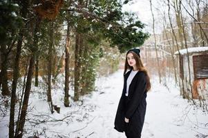 Fashionable long legs brunette model in long black cloak and hat outdoor at winter day. photo