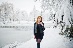 Red haired girl in fur coat walking at winter snowy park. photo