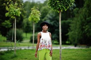 increíble mujer modelo afroamericana en pantalones verdes y sombrero negro posó en el parque. foto