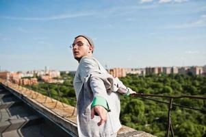 Dreamer stylish macho man in gray suit, hat and glasses posed on the roof. photo