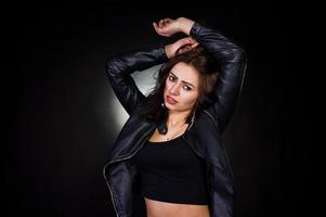 Studio portrait of sexy brunette girl in black leather jacket against black background. photo