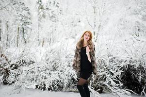 Red haired girl in fur coat walking at winter snowy park. photo