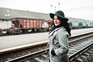 chica morena con abrigo gris con sombrero en la estación de tren. foto