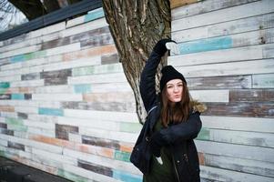 Young girl wear black headwear against wooden wall. photo