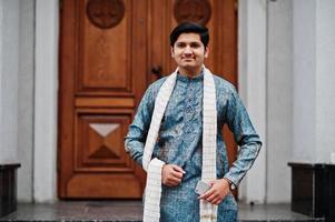 Indian man wear on traditional clothes with white scarf posed outdoor against door of building with mobile phone at  hand. photo