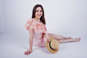 Portrait of a fashionable woman in pink dress sitting and posing with a hat on the floor in the studio. photo