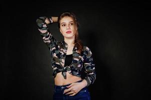 Handsome brunette girl wear military shirt and jeans, posing at studio against gray background. Studio model portrait. photo