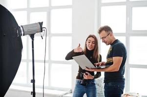 Photographer explaining about the shot to his assistant in the studio and looking on laptop. Teamwork and brainstorm. photo