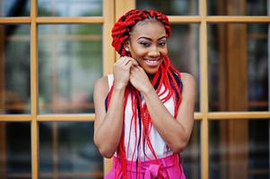 chica afroamericana de moda en pantalones rosas y rastas rojas posadas al aire libre. foto