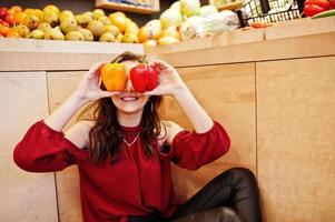 Girl in red holding two peppers on fruits store. photo