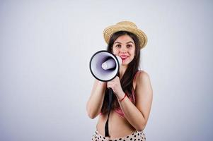 Portrait of a gorgeous young girl in swimming suit and hat talks into megaphone in studio. photo