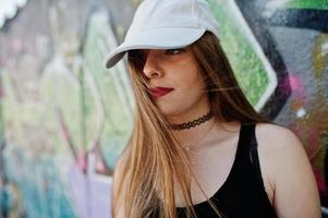 elegante chica hipster casual con gorra y jeans contra una gran pared de graffiti. foto