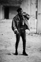 hombre afroamericano con chaqueta de jeans, boina y anteojos, fumando cigarro en una fábrica abandonada. foto