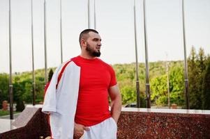 joven musculoso barbudo brutal vestido con traje deportivo blanco con camisa roja. foto