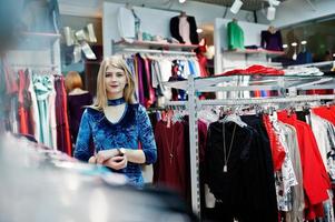 chica rubia con vestido azul en la boutique de la tienda de ropa. foto