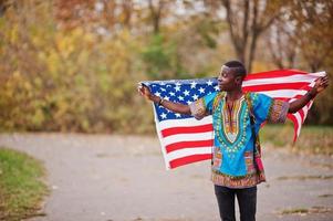 hombre africano en camisa tradicional africana en el parque de otoño con bandera de estados unidos. foto