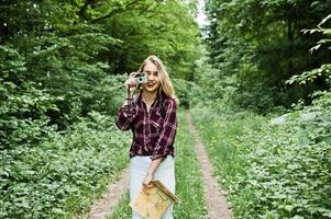 Portrait of a gorgeous young girl in tartan shirt taking pictures with camera in the forest. photo