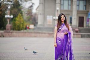 niña hindú india en el tradicional sari violeta posó en la calle contra las palomas. foto