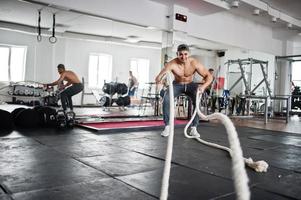 Fit and muscular arabian man working out with heavy ropes in gym. photo