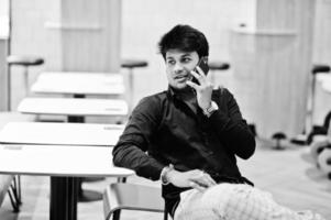 Stylish indian man sitting at fast food cafe, speaking on mobile phone and waiting his order. photo