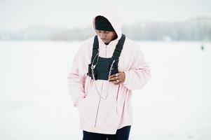 Elegante hombre afroamericano de estilo urbano con capucha rosa posado en un lago congelado en invierno. foto