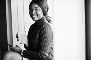 African american businesswoman drinking cocktail lemonade in cafe. Black girl having rest with mobile phone. photo