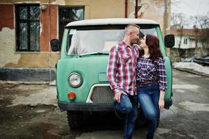 una pareja elegante usa una camisa a cuadros enamorada juntos contra una vieja minivan. foto