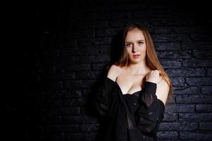 Studio shot of brunette girl in black blouse with bra and shorts against black brick wall. photo