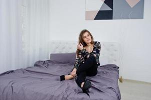 Handsome brunette girl wear military shirt, posing on bed at studio. Studio model portrait. photo