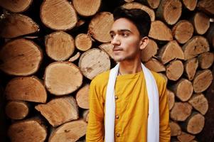 Indian stylish man in yeallow traditional clothes with white scarf posed outdoor against wooden stumps. photo