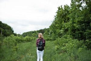 retrato de una atractiva chica rubia con camisa de tartán con mochila caminando por el campo. foto