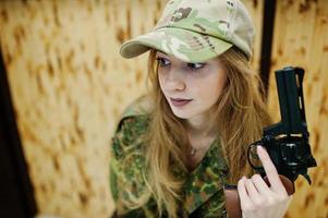 Military girl in camouflage uniform with revolver gun at hand against army background on shooting range. photo