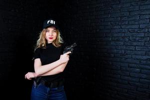 FBI female agent in cap and with gun at studio against dark brick wall. photo