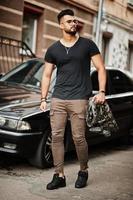 Awesome beautiful tall ararbian beard macho man in glasses and black t-shirt walking against business car. photo