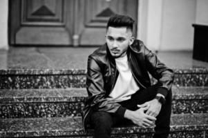 Stylish indian beard man at black leather jacket. India model posed sitting at streets of city. photo