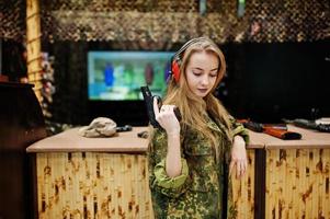 Military girl in camouflage uniform with gun at hand against army background on shooting range. photo