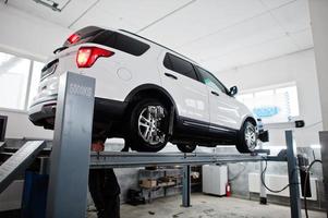 coche todoterreno americano en soporte para verificación de inclinación de alineación de ruedas en el taller de la estación de servicio. foto