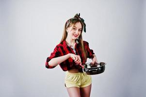 Young funny housewife in checkered shirt and yellow shorts pin up style with frying pan isolated on white background. photo