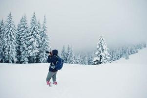 Man tourist photographer with backpack, at mountain with pine trees covered by snow. Beautiful winter landscapes. Frost nature. photo