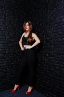 Handsome brunette girl wear on black and red high heels, posing at studio against dark brick wall. Studio model portrait. photo