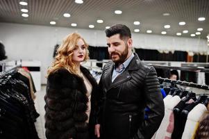 Elegance blonde girl in fur coat and stylish turkish man at the store of fur coats and leather jackets. photo