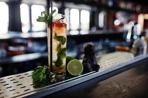 Alcoholic long cocktail with mint and lime in glass at bar table. photo