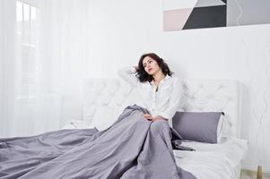 Studio portrait of brunette girl in white blouse lying on bed. photo