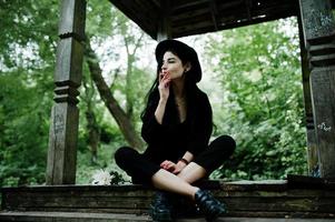 Sensual smoker girl all in black, red lips and hat. Goth dramatic woman smoking thin cigarette. photo