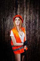 Engineer woman in orange protect helmet and building jacket against wooden background. photo