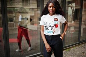 Stylish african american woman in printed t-shirt posed outdoor against window. photo