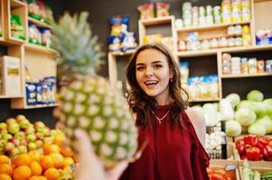 Girl in red holding pineapple on fruits store. photo