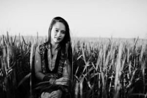 tierna niña india en sari, con maquillaje de labios violetas posada en el campo al atardecer. modelo indio de moda. foto