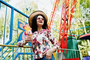 Portrait of brunette girl in pink glasses and hat with ice cream at amusement park. photo