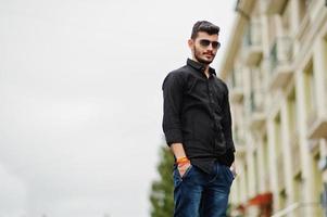 Indian stylish man at black shirt and sunglasses posed outdoor. photo